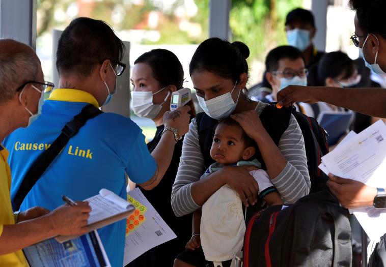 A mother and child get their temperatures checked as they prepare to board a bus back to Malaysia at a station in Singapore, November 29, 2021.