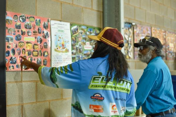 A woman points at a diagram on a posters on a brick interior wall. A man is listening.