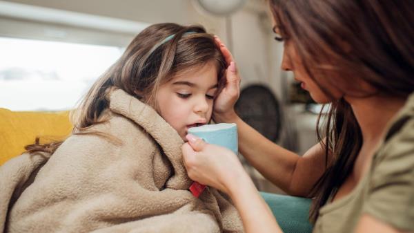 Mother helping young daughter drink from a mug.