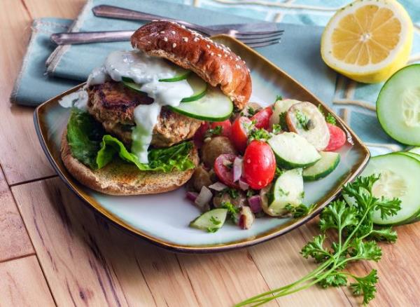 Greek stuffed turkey burger topped with cucumber slices and tzatziki yogurt sauce served with a fingerling Island potato side salad