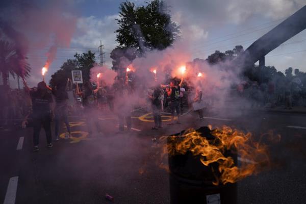 Pink smoke hovers in the air as a few people stand in a road under a blue sky.