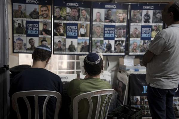 Three men with their backs to the camera, facing a display with many pictures of people, some of whom are wearing army uniforms.