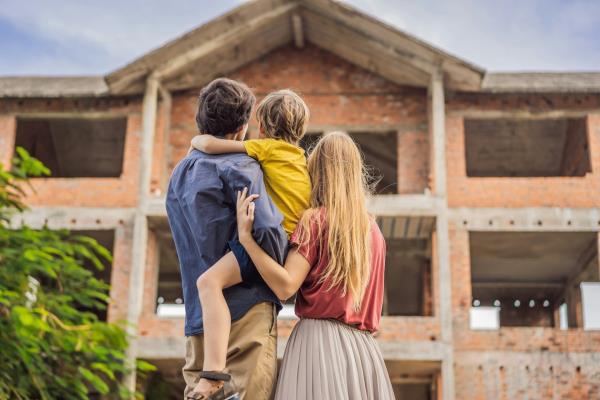 A young couple and their child look up at a home under construction