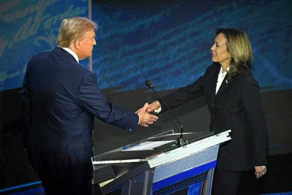 A man wearing a dark blue suit shakes hands with a woman wearing a black blazer.