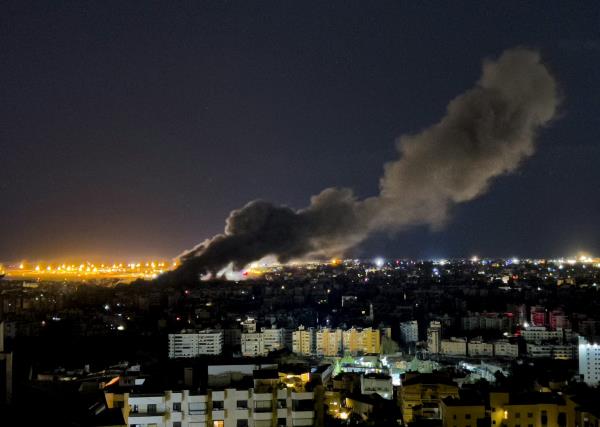 A cityscape at night with a large plume of smoke billowing up