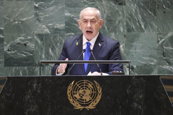 A man in a suit stands at a United Nations lectern and speaks