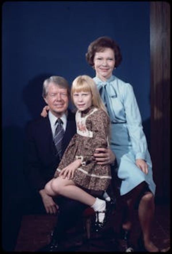 A man in a suit nurses his daughter and sits next to his wife.