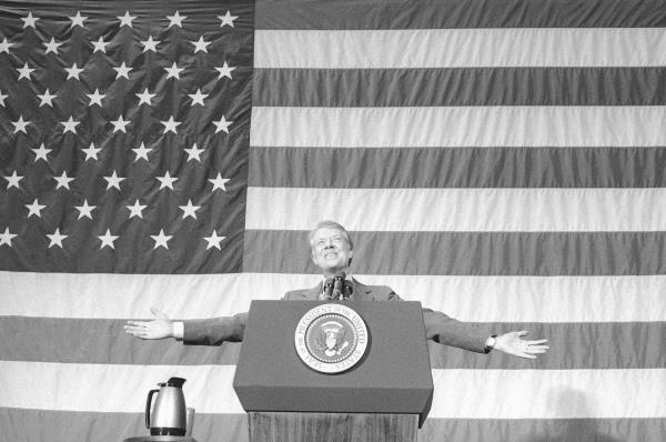 A man stands behind a lectern in front of a giant American flag