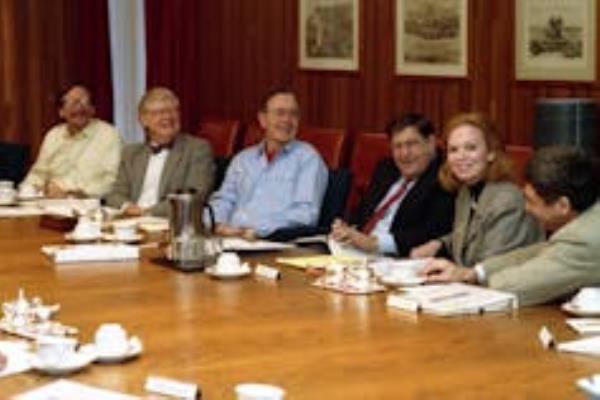 President Bush, smiling with his science advisors, seated at a long wooden table with coffee and briefing materials.