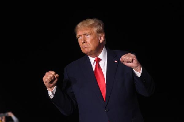 Trump, dressed in a suit, gestures on stage.