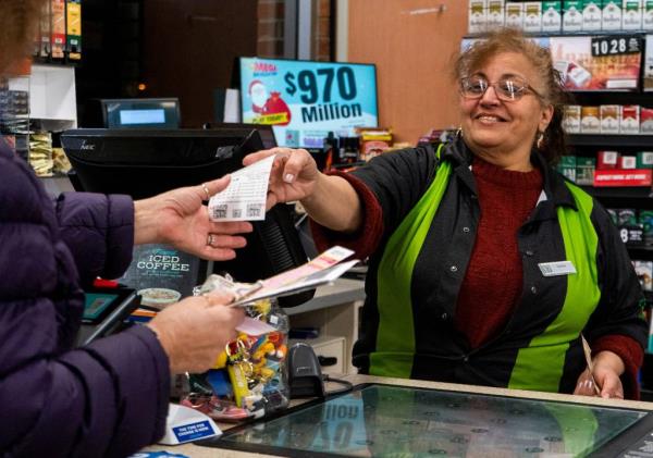 Samira Nusira hands a Mega Millions ticket, which is up to $970 Million, to a customer at the 7/11 in Levittown on Monday, Dec. 23, 2024.