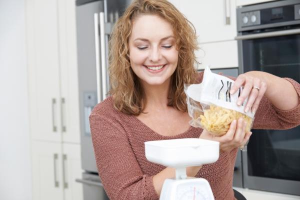 If you're weighing dry food, make sure to note it's 'uncooked' in your food tracker. Here, a woman pours dry pasta o<em></em>nto a scale.