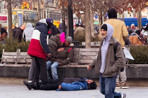 A woman attempting to wake up a man on a bench while another person lies down on the ground in The Hub on Nov. 27, 2024.