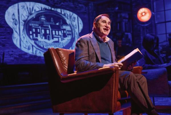 Richard Kind holding a binder on a chair