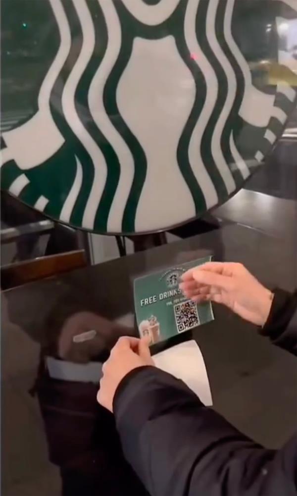 A person sticking a QR code reading "free drinks" on a Midtown Starbucks window.