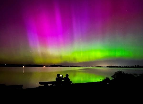 A man photographs the northern lights May 11 as he and a woman watch the celestial display from Perkins Peninsula Park on the shores of Fern Ridge reservoir west of Eugene, Oregon.