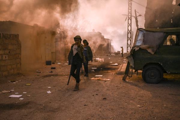 Men walk past smoke billowing after people looted and set fire at the Najha military housing complex in southeast Damascus on December 16, 2024. 