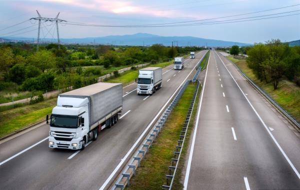 A series of white transportation trucks driving on a highway, illustrating commercial cargo transportation.